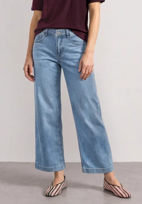 Mid Waist Jeansculotte met elastische tailleband Light Blue Random Washed Een persoon draagt lichtblauwe, wijduitlopende jeans en gestreepte, puntige flats tegen een neutrale achtergrond.