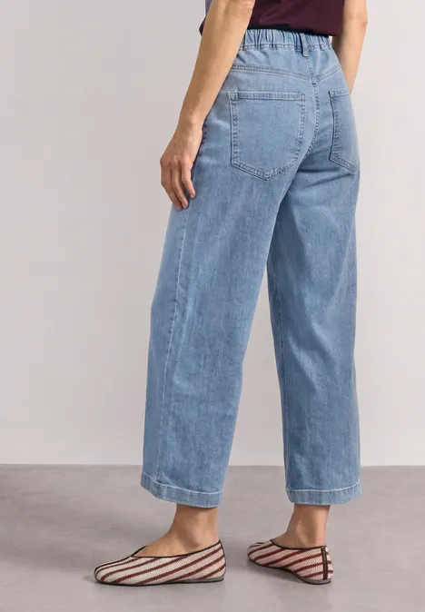 Mid Waist Jeansculotte met elastische tailleband Light Blue Random Washed Vrouw draagt losse lichtblauwe jeans tot de enkels en platte, gestreepte ballerina’s.