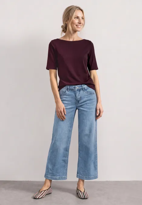 Mid Waist Jeansculotte met elastische tailleband Light Blue Random Washed Model draagt wijde jeans, bordeaux shirt en gestreepte platte sandalen voor neutrale achtergrond.