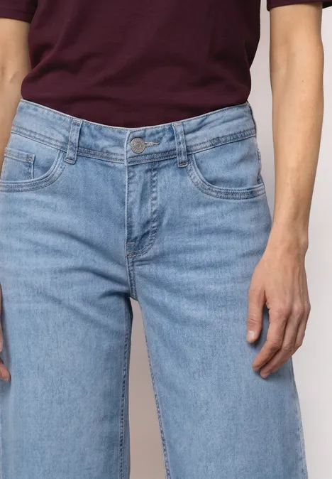 Mid Waist Jeansculotte met elastische tailleband Light Blue Random Washed Een persoon draagt lichtblauwe spijkerbroek en een bordeauxrood shirt, met focus op taille en handen.