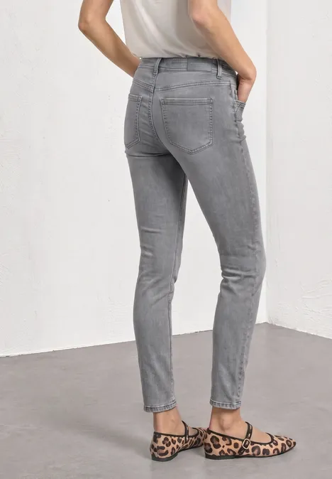 Mid Waist Slim Leg Jeans im Casual Fit Light Grey Random Washed Person von hinten in grauen Jeans und Leo-Ballerinas vor weißem Hintergrund.