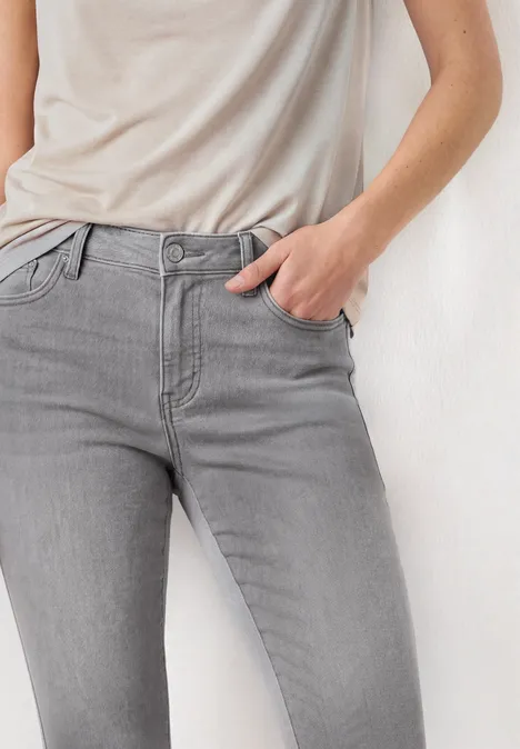 Mid Waist Slim Leg Jeans im Casual Fit Light Grey Random Washed Person mit grauen Jeans und leichtem beigen T-Shirt, Hand in Tasche.