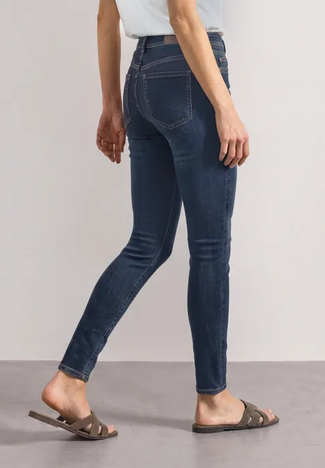 Mid Waist Slim Leg Jeans im Slim Fit Dark Blue Clean washed Dame trägt dunkelblaue Skinny-Jeans und flache braune Sandalen.