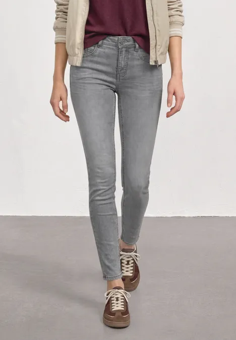 Mid Waist Slim Leg Jeans im Slim Fit Light Grey Random Washed Person trägt graue Skinny Jeans und braune Sneaker vor hellem Hintergrund.