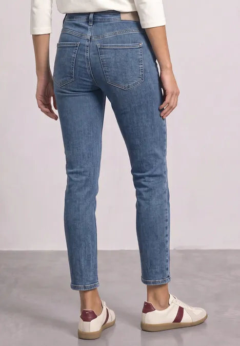 Person von hinten in schmal geschnittenen blauen Jeans und weißen Sneakers mit roten Details.