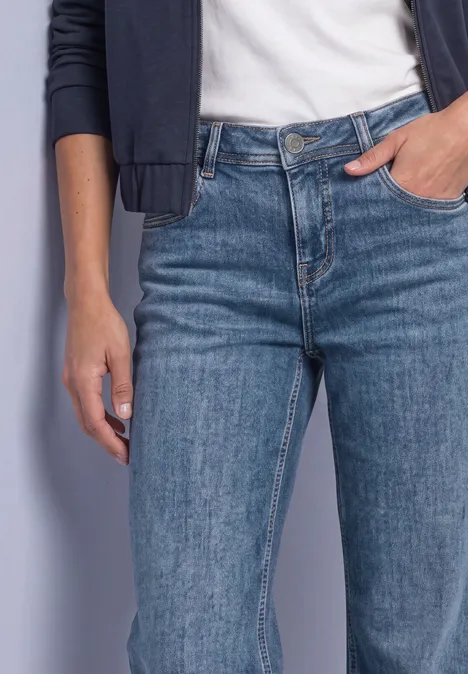 Frau trägt blaue Jeans, weißes T-Shirt und dunkle Jacke, Hand in Hosentasche