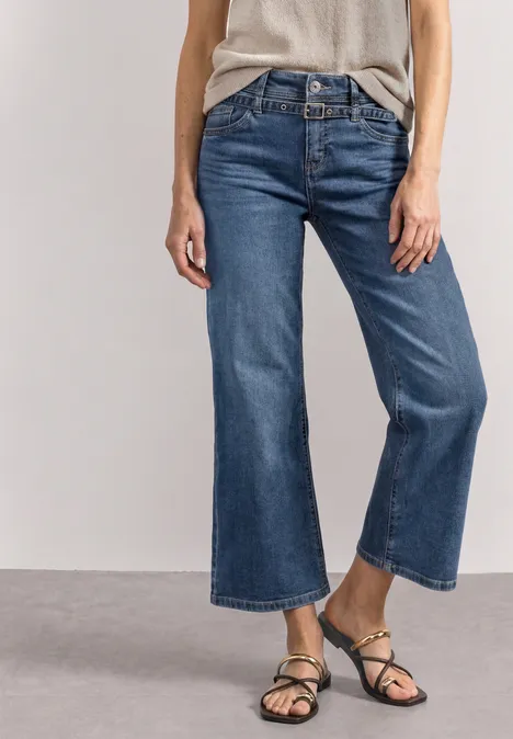 Jeans Culotte mit Gürteldetail Mid Blue Random Washed Person trägt weite, knöchellange blaue Jeans und schwarze Sandalen vor schlichtem, hellem Hintergrund.