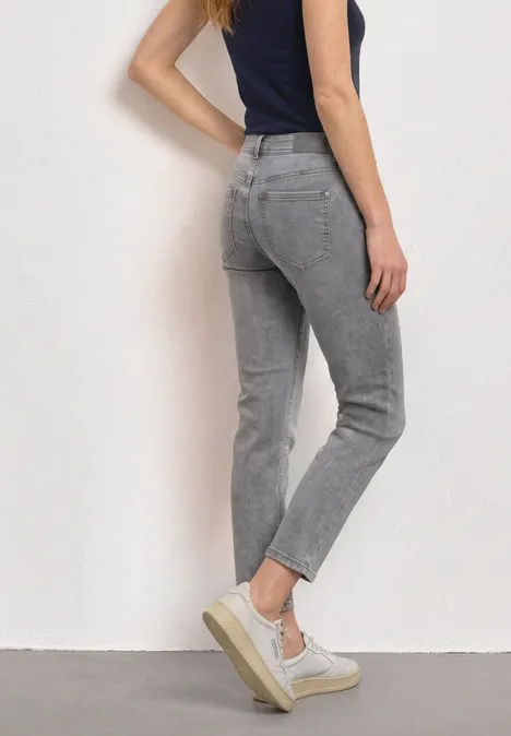 Mid Waist Straight Leg Jeans im Slim Fit Light Grey Random Washed Eine Frau trägt eine stilvolle graue Jeans und weiße Plateausneaker.