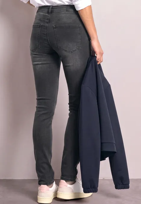 Persoon draagt zwarte skinny jeans en witte sneakers, houdt een donkerblauw jasje in de hand.