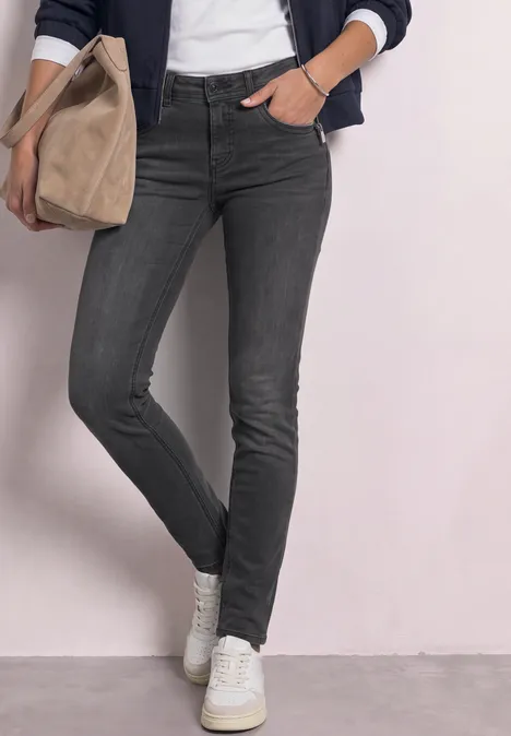 Vrouw in strakke grijze skinny-jeans, witte sneakers, met een beige canvas tas.