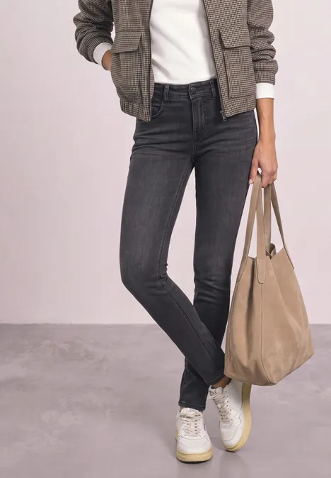 Persoon draagt zwarte skinny jeans, witte sneakers, een kaki bomberjack, een wit t-shirt en een beige tas.