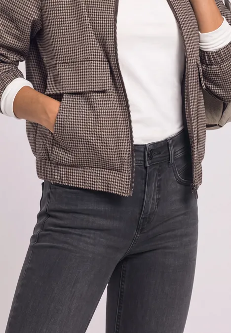 Bovenlichaam van een persoon met een geruite jas, witte top en donkerblauwe jeans.