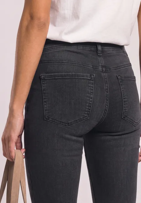 Close-up van een persoon van achteren in zwarte jeans en wit T-shirt, met een tas in de hand.