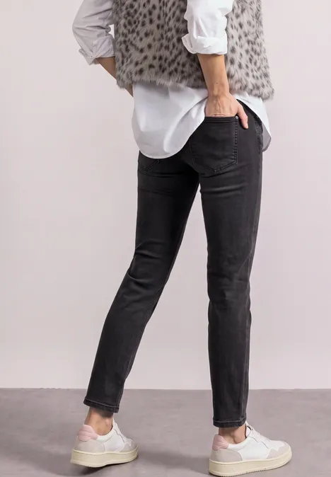 Persoon van achteren in zwarte slim-fit jeans, wit overhemd, grijs luipaardvest en witte sneakers.