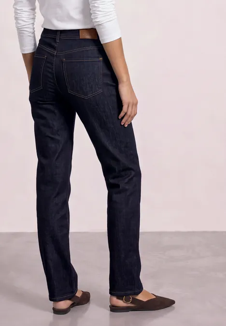 Achteraanzicht van persoon met donkere, rechte jeans en bruine ballerina's.