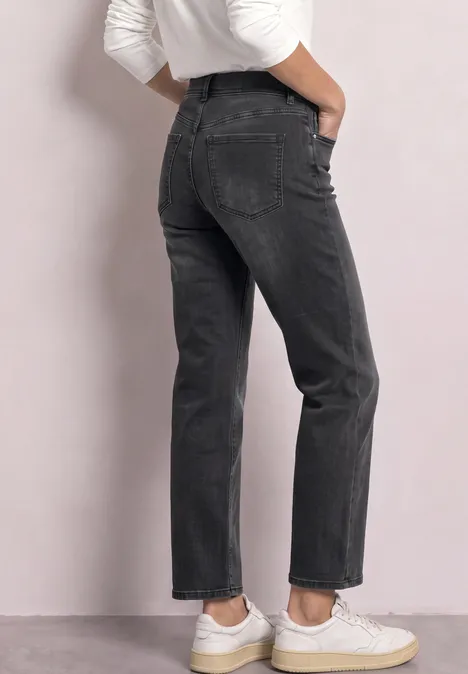 Vue arrière d’une personne portant un jean noir et des baskets blanches sur fond neutre.