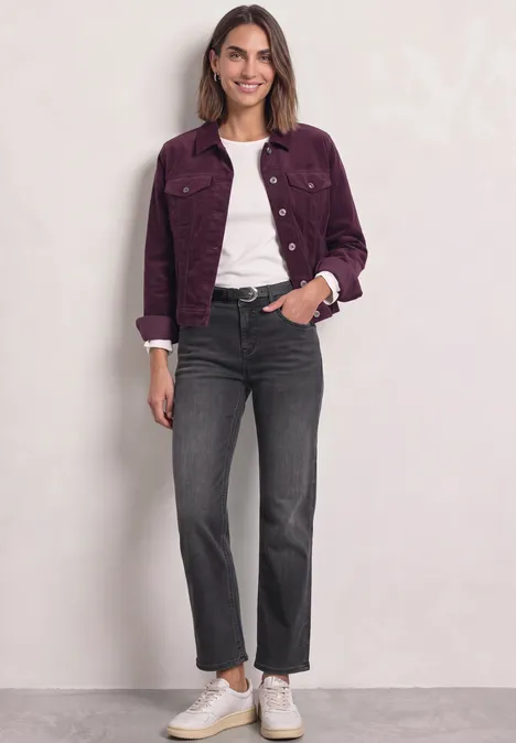 Femme en veste violette, tee-shirt blanc, jean noir évasé et baskets blanches devant un mur clair.