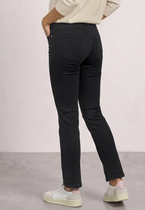 Vue arrière d’une personne portant un jean noir slim et des baskets blanches sur fond clair.
