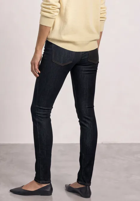 Jean taille moyenne Slim Leg, coupe slim Deep Rinse Washed Person steht von hinten in dunklen Skinny-Jeans, beigem Pullover und flachen Ballerinas.