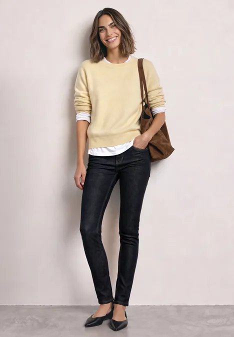 Jean taille moyenne Slim Leg, coupe slim Deep Rinse Washed Eine Frau trägt einen hellgelben Pullover über weißem Hemd, schwarze Jeans, spitze Ballerinas und eine braune Schultertasche.