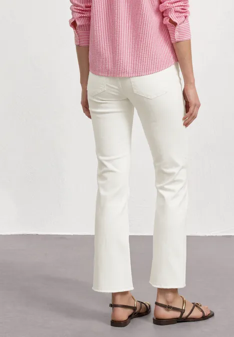 High Waist Flared Leg Jeans im Slim Fit Off White washed Frau trägt weiße, leicht ausgestellte Hose, rosa Pullover und flache Sandalen, Rückansicht.