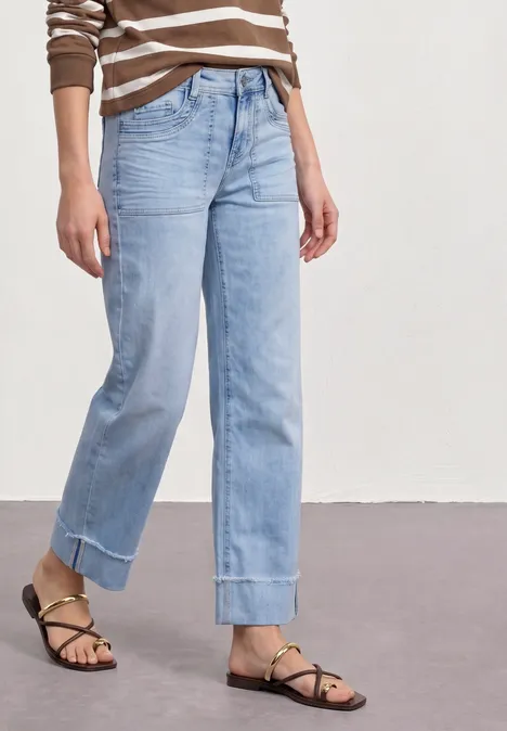 Vrouw draagt gestreepte top, lichte wijde jeans met omslag en zwarte sandalen met bandjes.