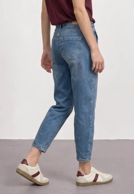 Person von hinten in lockeren blauen Jeans und Sneakers vor weißem Hintergrund.
