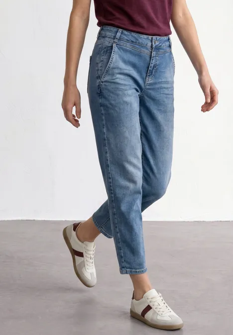 Eine Person trägt hoch taillierte, hellblaue Jeans und weiße Sneaker vor weißem Hintergrund.