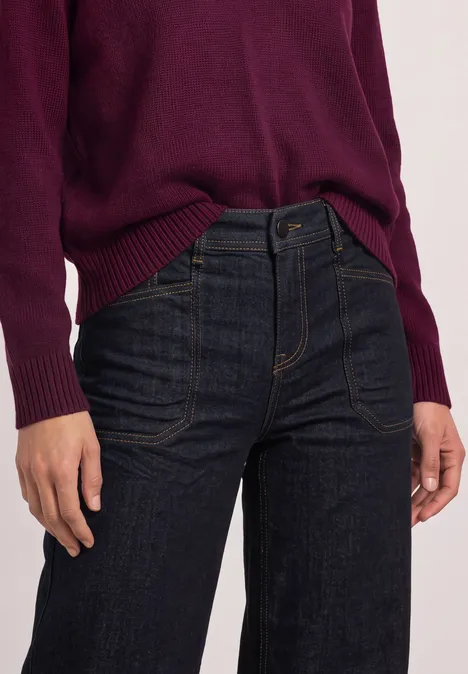 Iemand draagt een bordeauxrode trui en een donkerblauwe jeans.