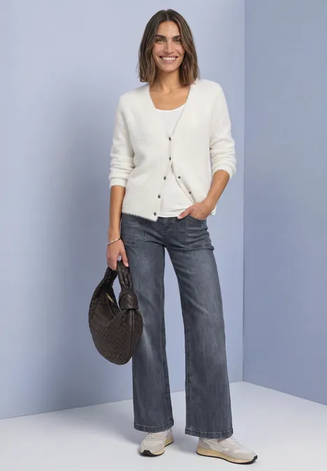 Mid Waist Wide Leg Jeans im Loose Fit Steel Grey Washed Frau mit weißer Strickjacke, grauen Jeans, Sneakern und runder Korbtasche.