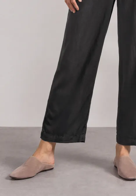 Person trägt schwarze weite Hose und graue Mules auf grauem Boden.