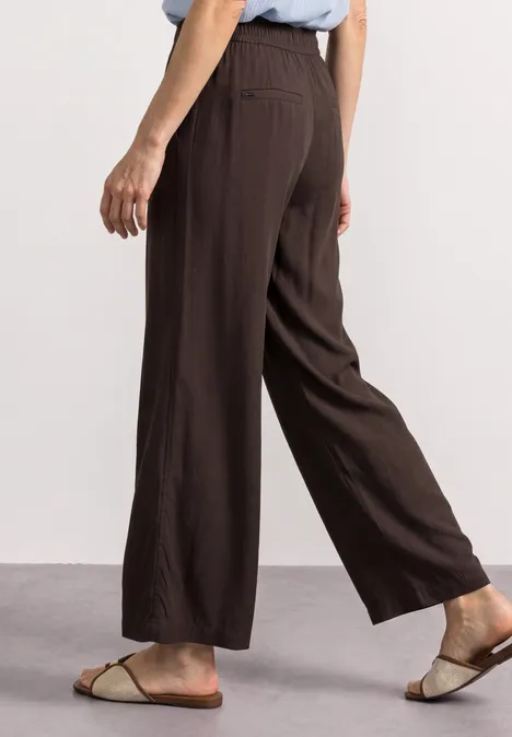Weite, braune Leinenhose in 7/8-Länge mit flachen Sandalen.