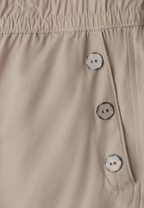 Beige Hose mit elastischem Bund und drei seitlichen Knöpfen.