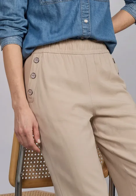 Damenhose in Beige mit seitlichen Knöpfen, kombiniert mit Jeansbluse.