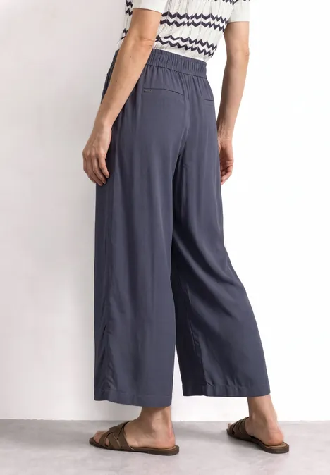 Frau trägt dunkelblaue, weite 7/8-Hose mit elastischem Bund und Taschen, dazu gestreiftes Oberteil und Sandalen.