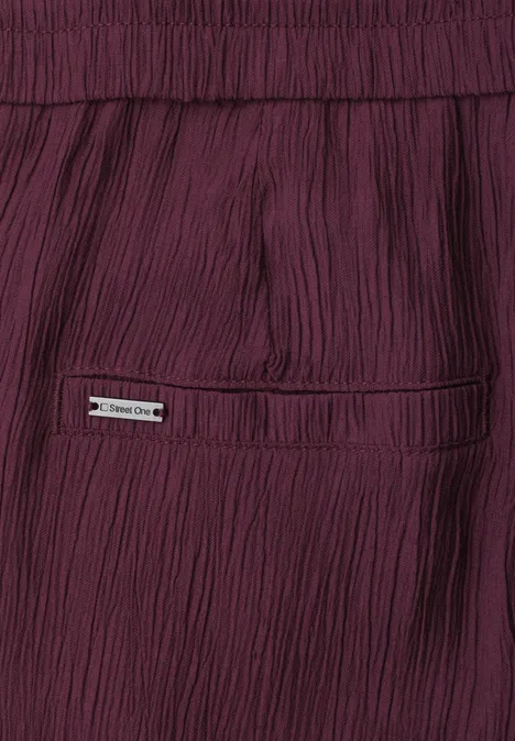 Nahaufnahme einer weinroten, plissierten Hose mit Gesäßtasche und kleinem Metall-Emblem