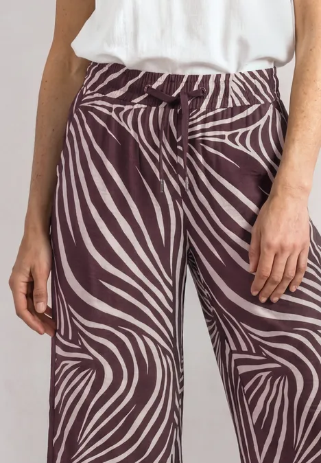 Wide Leg Hose mit Print und Gallonstreifen rustic rouge Nahaufnahme: Person trägt weiße Bluse und braun-weiße, zebramusternde, weite Hosen.