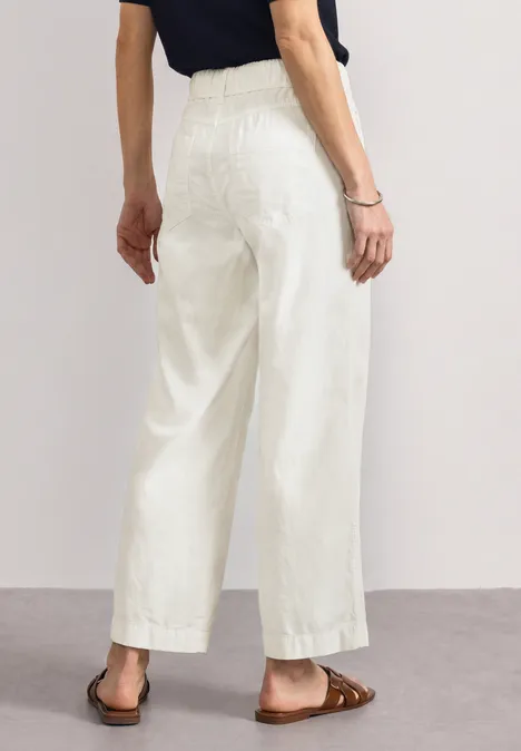 Person von hinten, trägt weiße, weite 7/8-Hose mit hohem Bund und braune Sandalen.