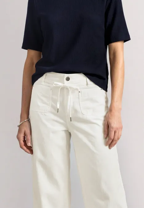 Frau in schwarzem Kurzarmshirt und weißen, weiten Hosen.