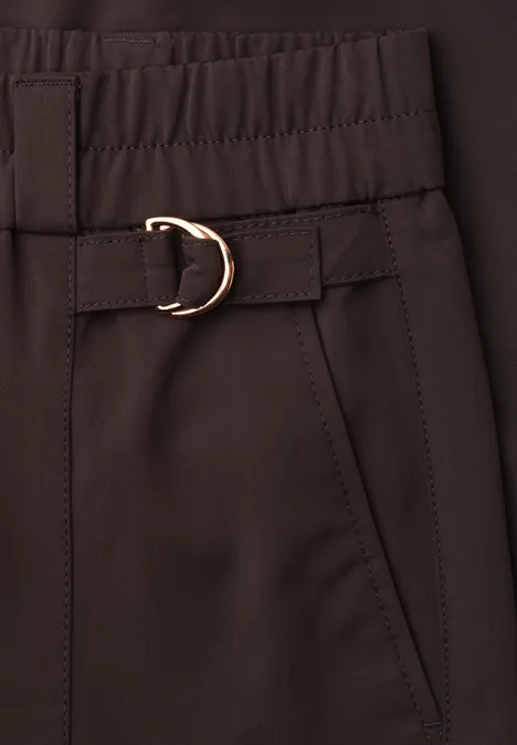 Nahaufnahme einer dunkelbraunen Hose mit elastischem Bund, Tasche und goldener D-Ring-Schnalle.