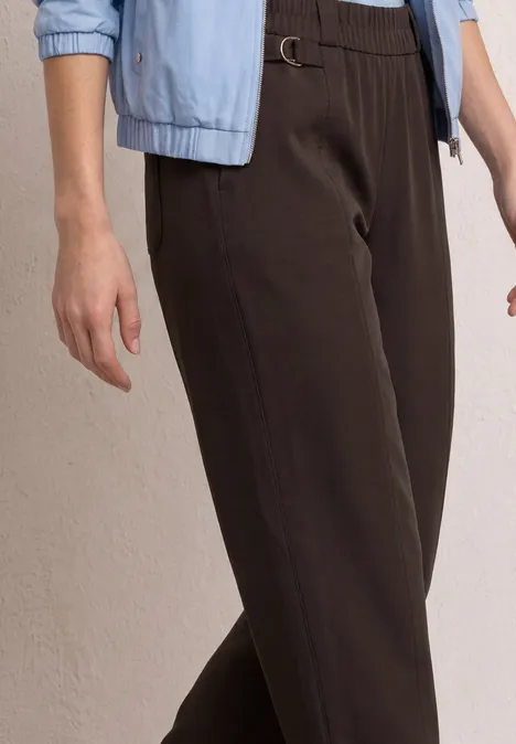 Person trägt hochgeschnittene, dunkelbraune Hose mit Gürtelschließe und hellblaue Jacke mit hochgekrempelten Ärmeln.