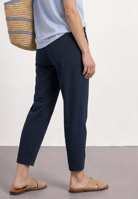 Frau trägt navyblaue Hose, hellblaues Top, Strohtasche und flache Sandalen.