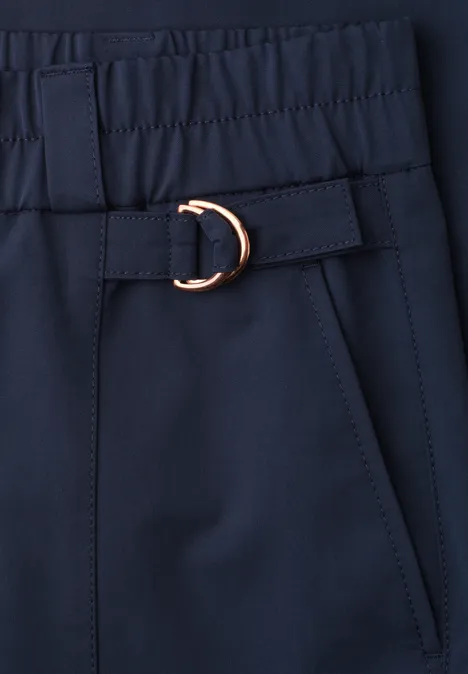 Nahaufnahme eines dunkelblauen Kleidungsstücks mit elastischem Bund, seitlicher Tasche und goldfarbenem D-Ring