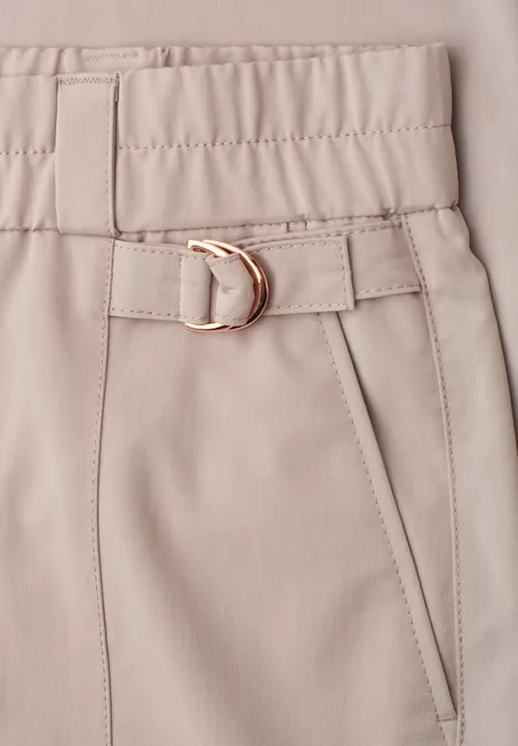 Beige Hose mit elastischem Bund, schmalem Gürtel mit goldener Metallschließe und seitlicher Eingrifftasche.