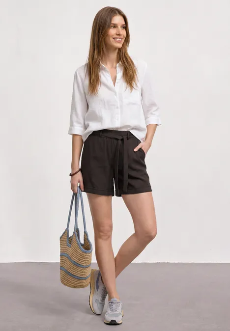 High Waist Shorts mit Gürtel espresso brown Eine Frau trägt eine weiße Bluse, schwarze Shorts, graue Sneaker und hält eine gestreifte Strohtasche.