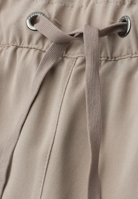 Nahaufnahme einer beigefarbenen Hose mit Tunnelzug und Metallösen am Bund.
