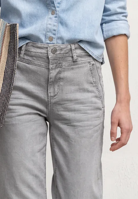 Hohe graue Jeans und hellblaues Jeanshemd, Torso mit Hand und Schultertasche zu sehen.