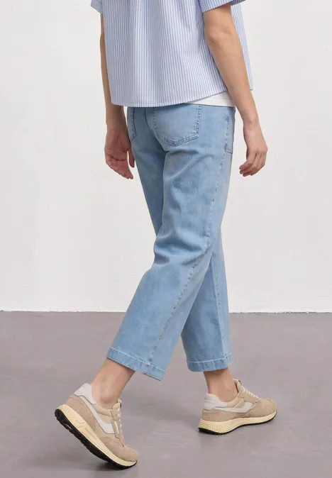 Mid Waist Jeans Culotte im Loose Fit Ultra Bleached Random Wash Person in hellblauen Jeans und beigen Sneakern, lässig stehend vor neutralem Hintergrund.