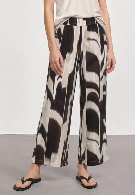Weit geschnittene Hose mit abstraktem Schwarz-Weiß-Muster, kombiniert mit Flip-Flops.