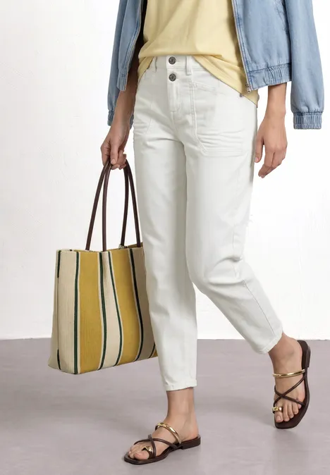 Person in weißen High-Waist-Jeans, Jeansjacke, gelber Streifentasche und braunen Sandalen.